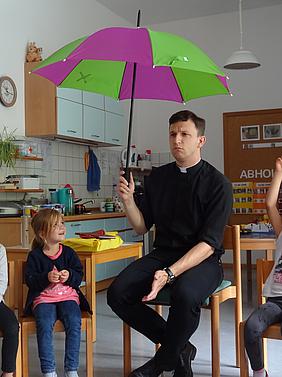Unter Gottes Schirm geborgen sein. Neupriester Michael Polster zu Besuch im Kath. Kindergarten Herz Jesu. Foto: Kath. Kita IN gGmbH/Grosse
